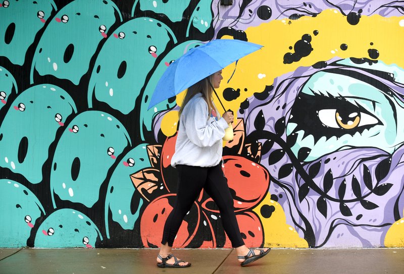 Allison Vincent, a recent graduate of the University of Arkansas, passes by a mural Tuesday on the east-facing side of The Academy at Frisco apartments in Fayetteville. The large mural, painted by artist Tiger Sasha in the summer of 2018, has two pieces with one 60 feet in length and other 80 feet in length. (NWA Democrat-Gazette/David Gottschalk)