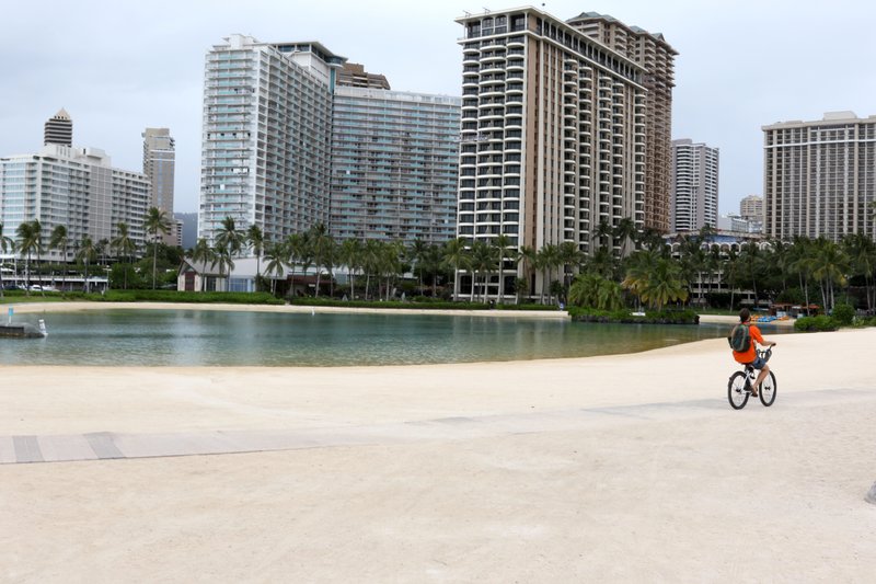 FILE - In this April 21, 2020, file photo, a man rides his bike on Waikiki Beach in Honolulu. The coronavirus pandemic has been particularly brutal to the tourism-dependent economies of Nevada and Hawaii, lifting the unemployment rate in both states to about one-quarter of the workforce. (AP Photo/Caleb Jones, File)