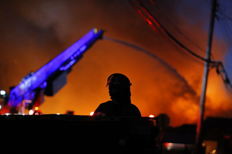 A police officer remains on watch as firefighters work during demonstrations Thursday, May 28, 2020, in St. Paul, Minn. Protests over the death of George Floyd, the black man who died in police custody, broke out in Minneapolis for a third straight night.