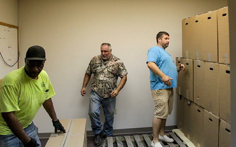 Jefferson County employees Terrence Thompson (from left) and Luke Eheman assist Jefferson County Election Administrator Sven Hipp in stacking boxes of voting machine stands Wednesday in a storage room at the Jefferson County Election Commission office.
(Arkansas Democrat-Gazette/Dale Ellis)