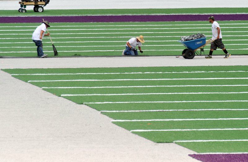 FILE -- Workers get ready to put down a strip of AstroTurf at Harmon Field at Fayetteville High School in July 2012, the last time the turf was replaced. The School District is preparing to replace the turf again this summer. (Arkansas Democrat-Gazette/MICHAEL WOODS)