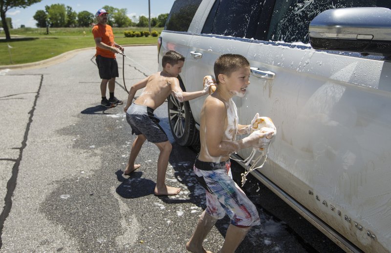 Preston Smith (from left), owner of Honey Badger Wrestling Club, helps wrestlers Jack Hooe, 12, and Mike Robertson, 10, wash a car Friday during a car wash benefit in the parking lot shared by The Joys of Swimming and Honey Badger Wrestling Club in Bentonville. The two businesses teamed to hold the free car wash with donations encouraged to help keep their bills paid during the covid-19 pandemic. Both businesses pened earlier in May under Arkansas Department of Health guidelines for gyms. The Joys of Swimming is offering families the ability to reserve the pool for themselves in 45 minute blocks and the wrestling club is largely limiting contact activities to wrestlers within the same family. Bonnie Adams, owner of The Joys of Swimming, said the covid-19 closings have "drastically" affected her business. Both owners said they have applied for financial assistance through the Coronavirus Aid, Relief and Economic Security Act and are waiting to find out if they'll receive aid. Limits on the percentage of funds through the Paycheck Protection Program that can be used for non-payroll costs can be a hurdle to some small businesses with few employees. Adams said she has staff instructors, but that her biggest operating expense is rent. Smith said all of his coaches are volunteers and nearly all of his expenses are in the facility. (NWA Democrat-Gazette/Ben Goff)