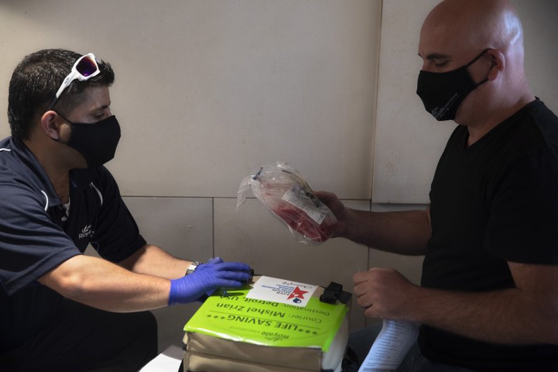 In this May 19, 2020 photo, Israeli courier Mishel Zrian, right, receives bone marrow at Ben Gurion airport near Tel Aviv, Israel. Over the past two months, as air travel has ground to a halt, Mishel Zrian has criss-crossed the Atlantic and the United States dozens of times, sleeping in empty airports and unable to return home to see his family in Israel, all in a race against time to deliver life-saving transplants. (AP Photo/Sebastian Scheiner)