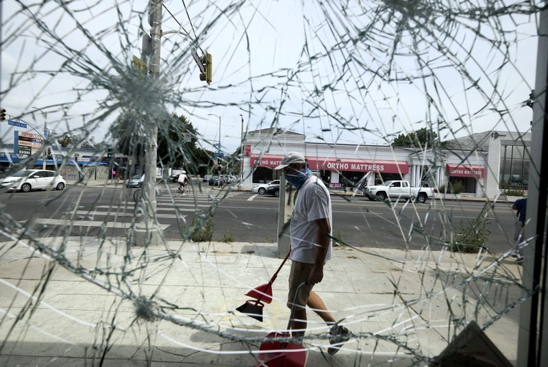 A volunteer sweeps up broken glass behind a shattered store glass door, Sunday, May 31, 2020, in Los Angeles, following a night of unrest and protests over the death of George Floyd, a black man who was in police custody in Minneapolis. Floyd died after being restrained by Minneapolis police officers on May 25. (AP Photo/Ringo H.W. Chiu)