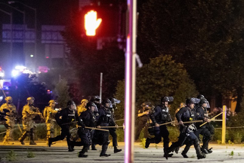 Police and Kentucky National Guard troops chase protesters as they flee toward a fence Sunday, May 31, 2020, in a parking lot at the corner of East Broadway and South Brook Street in downtown Louisville, Kentucky. (Max Gersh/The Courier Journal via AP)