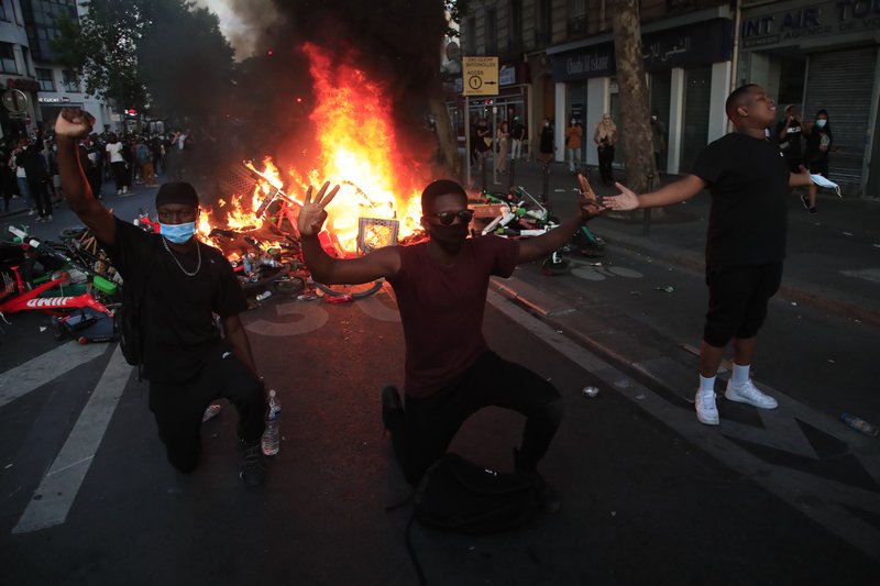 Protesters kneel and react by a burning barricade during a demonstration Tuesday, June 2, 2020 in Paris. Paris riot officers fired tear gas as scattered protesters threw projectiles and set fires at an unauthorized demonstration against police violence and racial injustice. Several thousand people rallied peacefully for two hours around the main Paris courthouse in homage to George Floyd and to Adama Traore, a French black man who died in police custody. (AP Photo/Michel Euler)