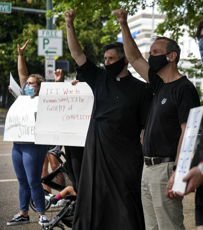 Father Marcus Emmons of Christ Anglican Church, left, and Father Robert Odom of St. Luke's Episcopal Church raise their fists in solidarity during Tuesday's protest in Hill Wheatley Plaza. - Photo by Grace Brown of The Sentinel-Record