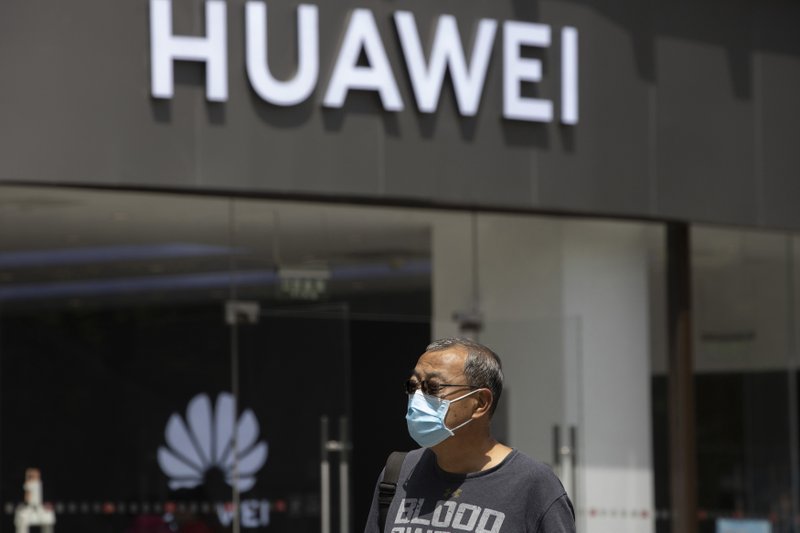 FILE - In this May 18, 2020, file photo, a man wearing a face mask to protect against the coronavirus walks past a Huawei retail store in Beijing. One of China&#x2019;s biggest tech companies has criticized the Trump administration for &#x201c;politicizing business&#x201d; after it slapped export sanctions on 33 more Chinese enterprises and government entities. The announcement expanded a U.S. campaign against Chinese companies Washington says might be security threats or involved in human rights abuses. Beijing criticized curbs imposed earlier on tech giant Huawei and other Chinese companies but has yet to say whether it will retaliate. (AP Photo/Ng Han Guan, File)