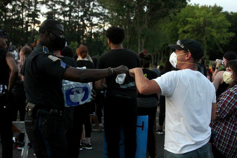 Arkadelphia police Sgt. Alvin Johnson fist-bumps a protester while handing out water at Tuesday night's protest at the future site of the Dr. Martin Luther King Jr. Memorial Park in Arkadelphia. - Photo by James Leigh of The Sentinel-Record