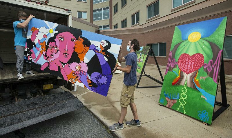 Ian Osgood (left) and Logan Auffet with Lightworks Events in Springdale unload a painting Thursday by artist Octavio Logo at Northwest Medical Center-Bentonville. The men were installing temporary murals by nine local artists that are part of the Social Connecting Campaign by Crystal Bridges Museum of American Art and the Momentary. The campaign seeks to support those most vulnerable to the effects of isolation during the covid-19 pandemic. People have been taking home postcards with line art versions of the paintings to color and mail to hospital patients and senior living facilities. The murals are on a tour of the same facilities throughout Northwest Arkansas, set up each day outside for residents and guests to enjoy. Go to nwaonline.com/200605Daily/ to see more photos.
(NWA Democrat-Gazette/Ben Goff)
