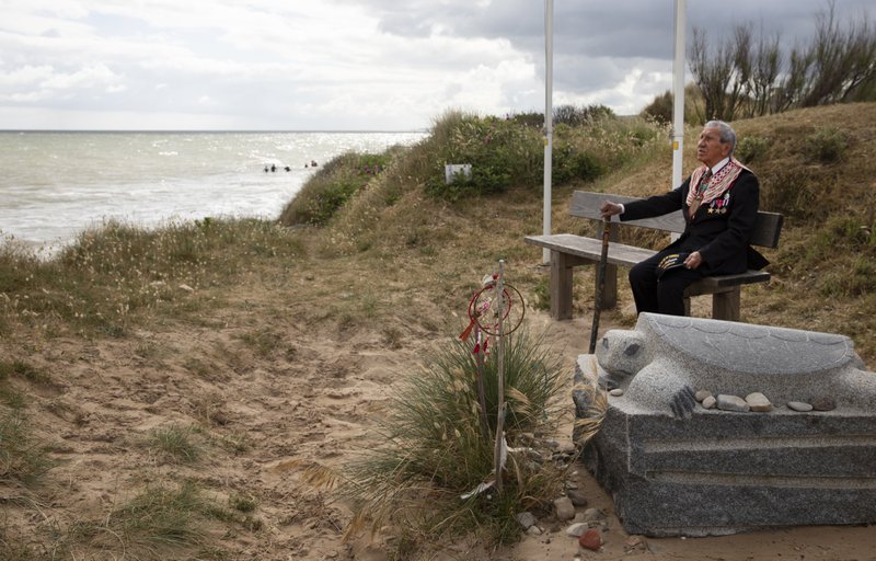 World War II D-Day veteran and Penobscot Elder from Maine, Charles Norman Shay sits on a bench next to his memorial stone at Omaha Beach prior to a ceremony in Saint-Laurent-sur-Mer, Normandy, France, on Friday. Today's anniversary of D-Day will be one of the loneliest remembrances ever, as the coronavirus pandemic is keeping almost everyone away, from government leaders to frail veterans who might not get another chance for a final farewell to their unlucky comrades. - AP Photo/Virginia Mayo