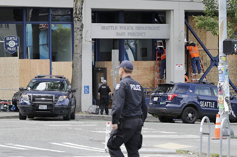 Workers put up plywood to cover the windows of a Seattle police precinct Monday. (AP/Elaine Thompson) 