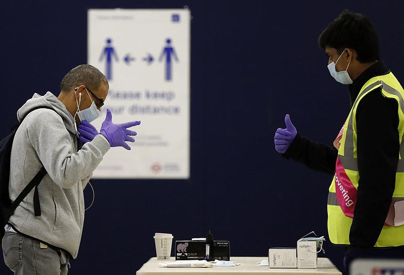 A London Underground worker (right) hands over a free mask, gloves and hand sanitizer to a pas- senger Tuesday at London’s Baker Street station. Masks will become compulsory on London’s public transportation service starting Monday. More photos at arkansasonline.com/610virus/. (AP/Frank Augstein) 