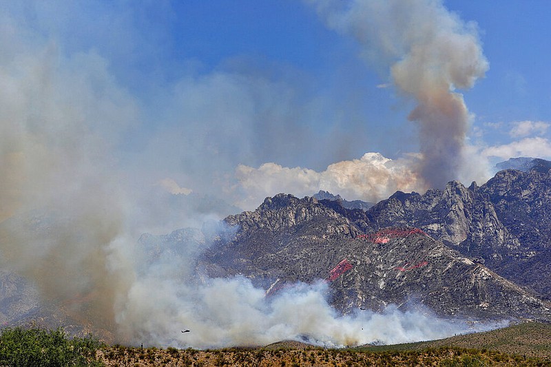 A helicopter is visible at lower left as it and other wildfire air attack crews continue to battle the Bighorn Fire along the western side of the Santa Catalina Mountains on Friday, June 12, 2020, in Oro Valley, Ariz. (AP Photo/Matt York)


