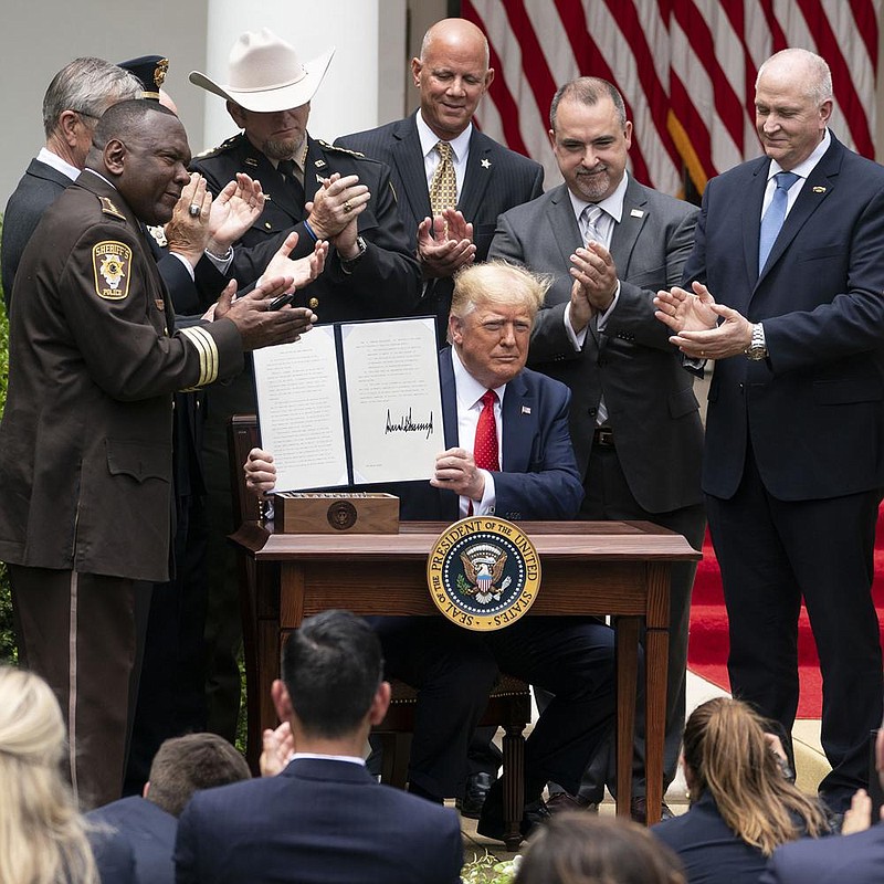 As law enforcement officials gather around him Tuesday in the White House Rose Garden, Presi- dent Donald Trump displays his signed executive order on safe policing for safe communities. More photos at arkansasonline.com/617police/. (The New York Times/Doug Mills) 