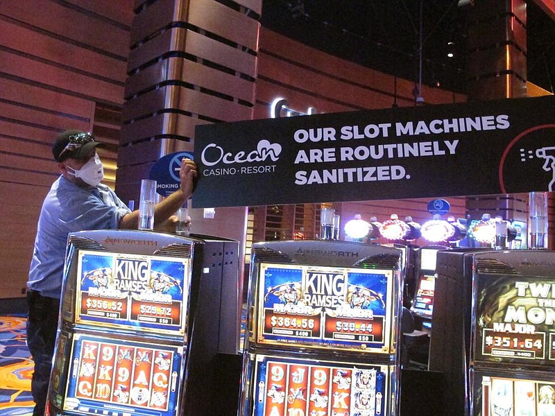 A worker at the Ocean Casino Resort in Atlantic City, N.J., installs a sign earlier this month about slot machines being sanitized to prevent the spread of the coronavirus. (AP/Wayne Parry) 
