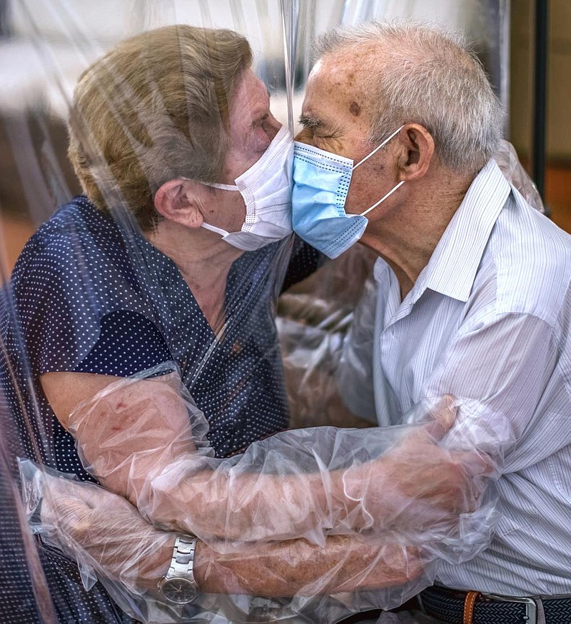 Agustina Canamero, 81, and Pascual Perez, 84, embrace and kiss Monday through a plastic screen at a nursing home in Barcelona, Spain, after a nationwide coronavirus lockdown separated them for 102 days. The couple have been married for 59 years. More photos at arkansasonline.com/623virus/. (AP/Emilio Morenatti) 