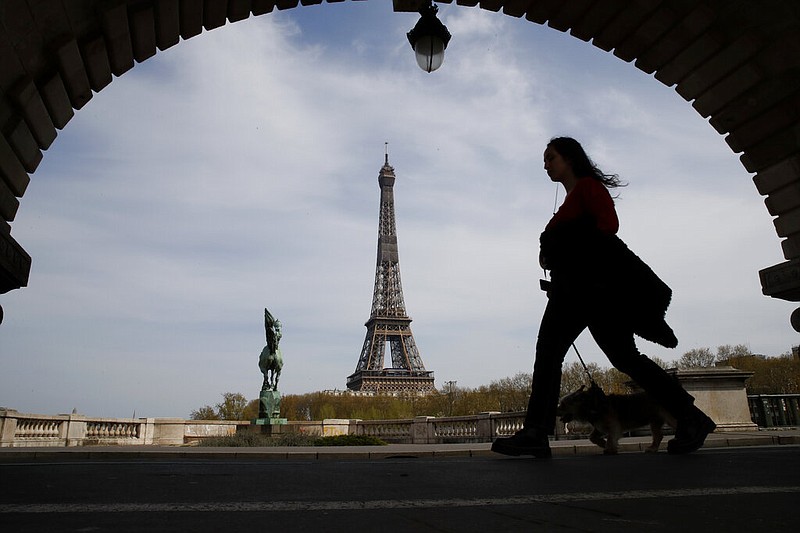 FILE - In this Tuesday, April 7, 2020 file photo, a woman walks her dog on a Paris bridge, with the Eiffel tower in background, during a nationwide confinement to counter the COVID-19. The European Union announced Tuesday, June 30, 2020 that it will reopen its borders to travelers from 14 countries, but most Americans have been refused entry for at least another two weeks due to soaring coronavirus infections in the U.S. (AP Photo/Christophe Ena, File) story.lead_photo.caption