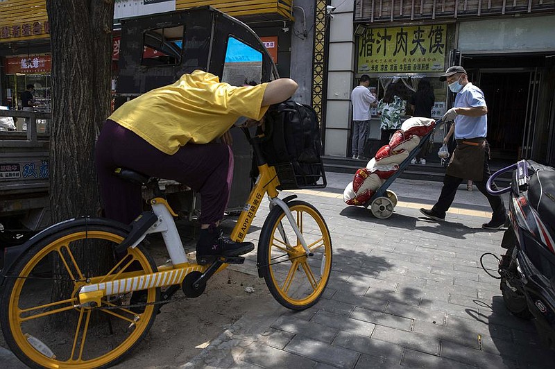 A delivery man passes a food stall Wednesday in Beijing. Three months after China started a postpandemic reopening of its economy, businesses are struggling to lure back consumers.
(AP/Ng Han Guan)