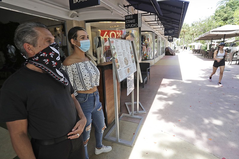 Restaurant workers Alvyn Lopez, left, and Maria Lindo watch for customers as they stand outside Aura at Books & Books, Monday, July 6, 2020, on Miami Beach, Florida's famed Lincoln Road. In Miami-Dade County, population 2.7 million, Mayor Carlos Gimenez ordered the closing of restaurants and certain other indoor places, including vacation rentals, seven weeks after they were allowed to reopen. Beaches will reopen on Tuesday after being closed over the weekend. 