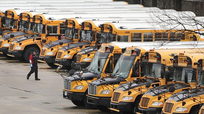 A worker passes public school buses parked at a depot in Manchester, N.H., in April. As school districts cope with the pandemic, some are worried about being able to afford added supplies, including masks and more buses. (AP/Charles Krupa) 
