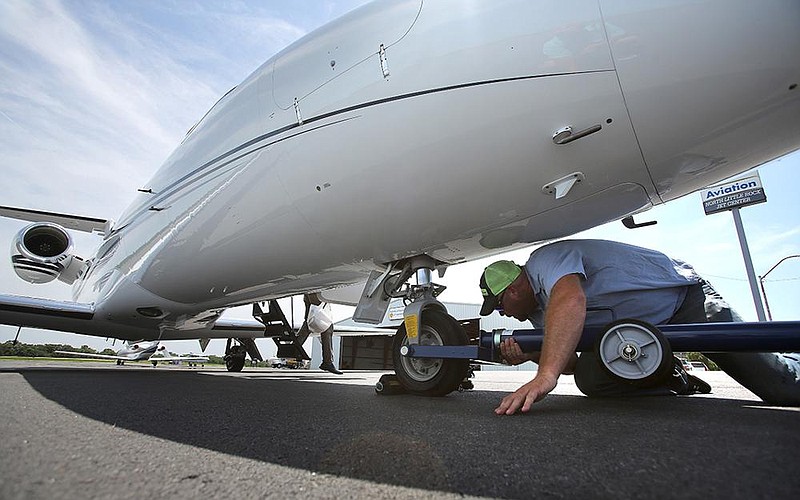 Josh Holmes, a line service technician, hooks up the landing gear of a jet to tow it into the hangar after it landed Friday at the North Little Rock Municipal Airport. (Arkansas Democrat-Gazette/Thomas Metthe) 
