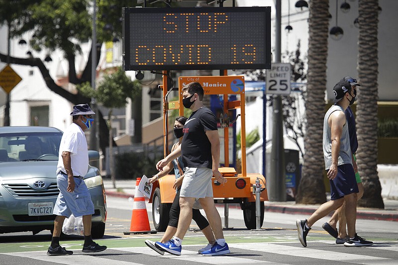 Pedestrians wear masks as they cross a street amid the coronavirus pandemic Sunday, July 12, 2020, in Santa Monica, Calif. A heat wave has brought crowds to California's beaches as the state grappled with a spike in coronavirus infections and hospitalizations. (AP Photo/Marcio Jose Sanchez)

