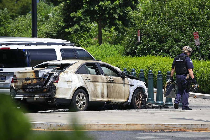 A bomb technician walks past an automobile that was set on fire near the Supreme Court in Washington on Wednesday, July 15, 2020. Police said that the young man who set the police car on fire suffered serious burns in the process.