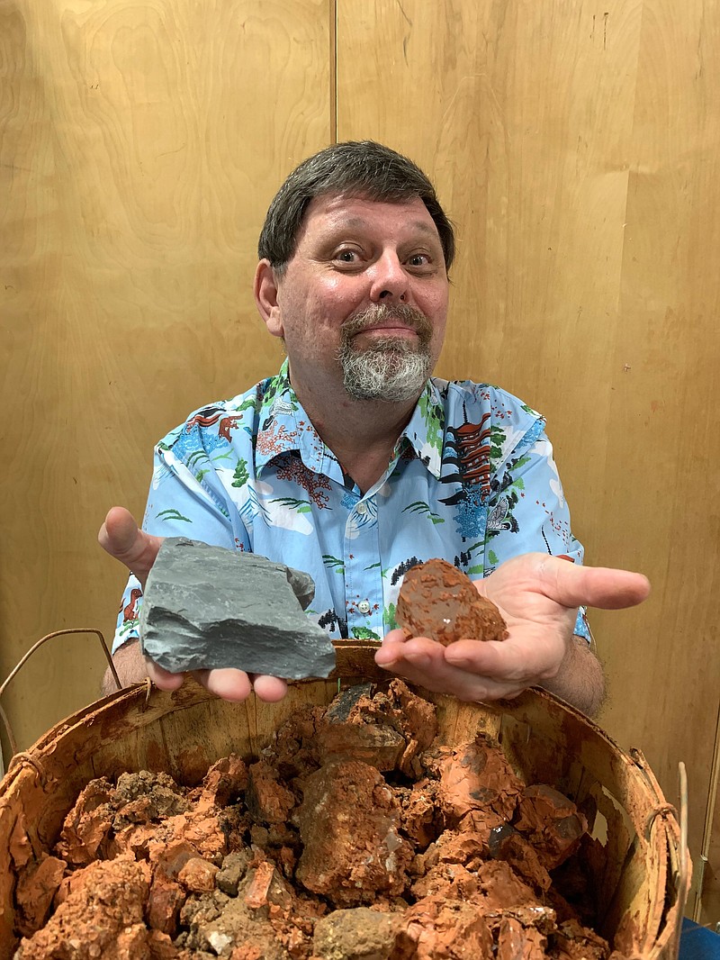 Mike Means will host crystal and fossil digging workshops over the next two weeks at the South Arkansas Arts Center. In his right hand is an example of the rock samples students will try to find fossils in, and in his left hand is an example of the red clay students will search for crystals in. (Contributed)