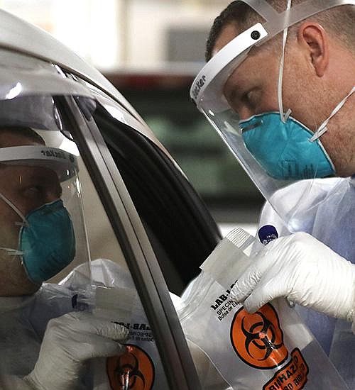 Andrew Becker talks to a motorist Friday after administering a covid-19 test at the University of Arkansas for Medical Sciences drive-thru testing site.
(Arkansas Democrat-Gazette/Thomas Metthe)