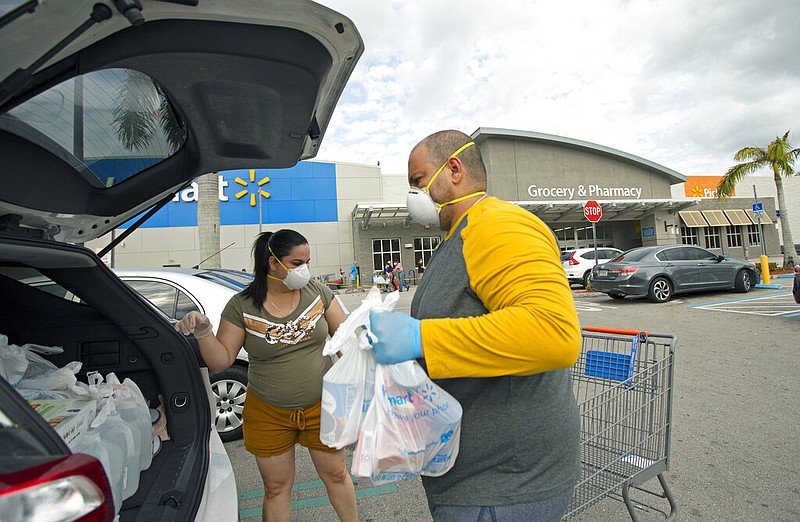 Joel Porro and Lizz Hernandez wear gloves and protective masks as they put bags in the trunk of their car after shopping at a Walmart Supercenter in Miami, Fla., in this April 5, 2020, file photo.