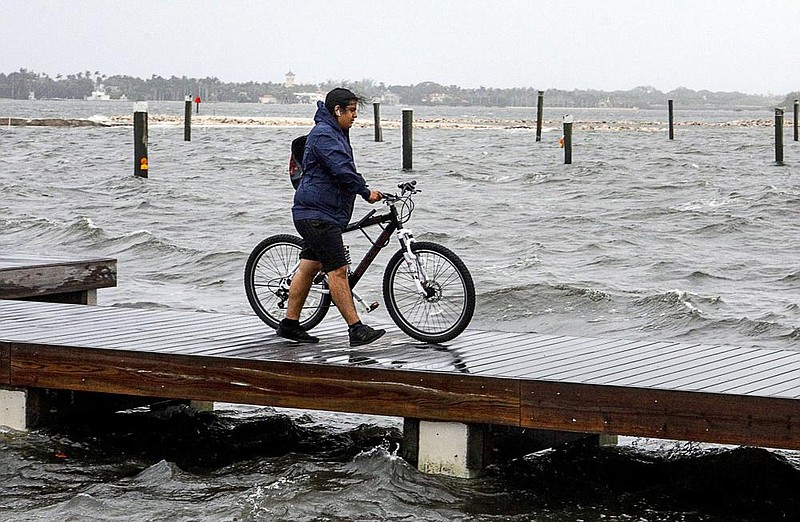 Ricardo Martinez walks his bike across a pier Sunday on the Intracoastal waterway in heavy winds from Isaias. Video at arkansasonline.com/83isaias/ (AP/The Palm Beach Post/Damon Higgins) 