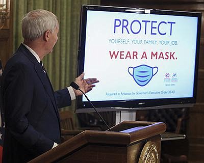 Gov. Asa Hutchinson, at his coro- navirus briefing Monday in Little Rock, presents mask-related signs that are available for busi- nesses. More photos at arkansas online.com/84governor/. (Arkansas Democrat-Gazette/ Staton Breidenthal) 