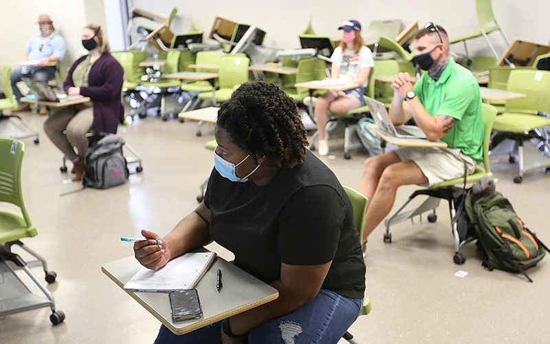 Dannie Brown, a senior at the University of Arkansas, Fayetteville, takes notes Monday during a history class that’s part of the university’s Intersession term. Students and professors are expected to wear masks, and classrooms on campus have been arranged with physically distanced seating. (NWA Democrat-Gazette/David Gottschalk) 