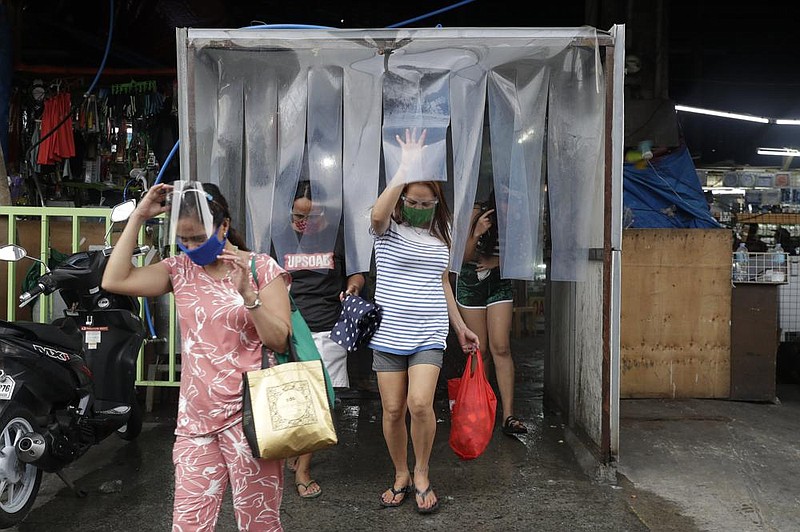 Women leave a disinfecting area Monday after stocking up at a Quezon, Philippines, market ahead of stricter lockdown measures. Philippine President Rodrigo Duterte is reimposing a moderate lock- down in the capital and outlying provinces after medical groups appealed for the move as corona- virus infections surge. More photos are available at arkansasonline.com/84virus/ 
(AP/Aaron Favila) 