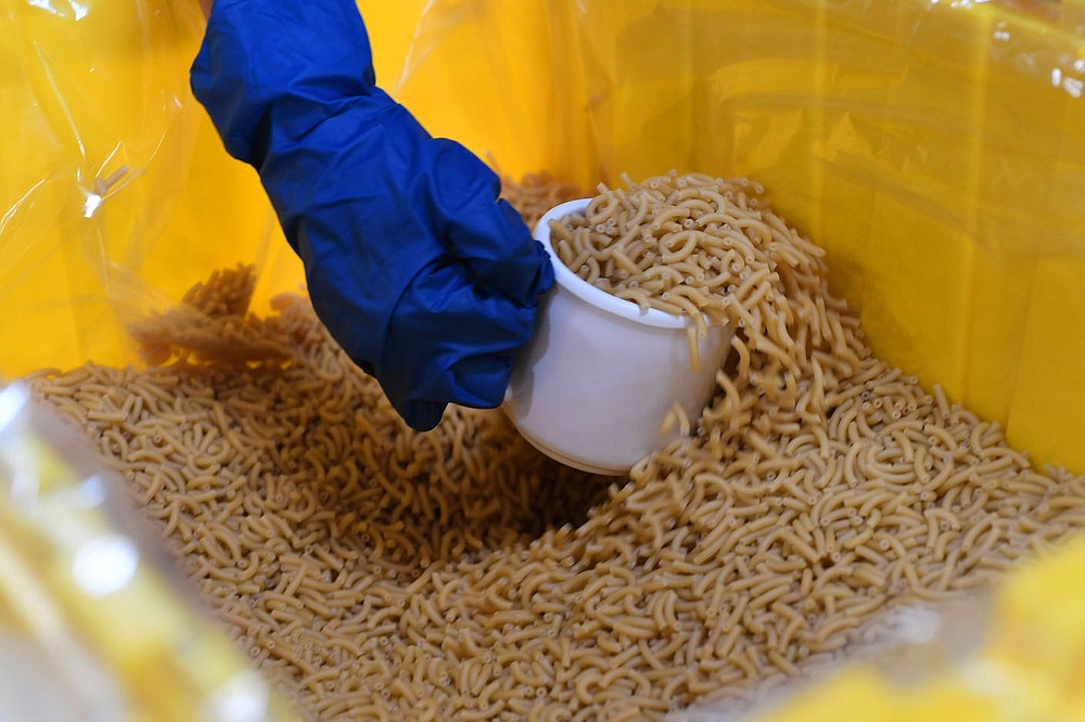 Melnicki scoops dry noodles while helping assemble food packs at The Pack Shack.
(NWA Democrat-Gazette/J.T. Wampler)