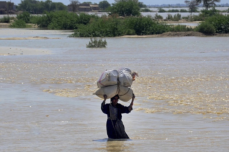 A woman carries sacks of wheat and household goods Sun- day as she wades through a ooded area of Dadu in Pakistan’s Sindh province. (AP/Pervez Masih) 