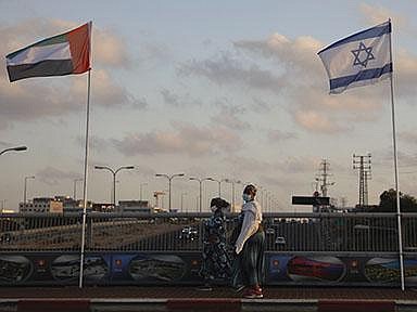 Women walk past flags for the United Arab Emirates and Israel on Sunday at the Peace Bridge in Netanya, Israel. The UAE flag was displayed to celebrate last week’s announcement on the countries’ diplomatic relations. (AP/Ariel Schalit) 