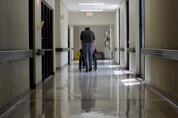The activity director at the Windcrest Health and Rehab Inc. nursing home in Springdale pushes a resident down a hall in this July 29, 2013, file photo.