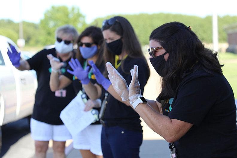 Art teacher Olivia Slone (right) and other teachers at Tucker Elementary School in Lowell wave to students and their families Thurs- day during a back-to-school drive-thru event to deliver school supplies and meet one another. Staff members and students will wear masks when school begins Monday and take unmasked outdoor breaks throughout the day. It’ll be a challenge to keep young kids masked, Slone said, but “we’ll do our best.” More photos at arkansasonline.com/823masks/. 
(NWA Democrat-Gazette/Dan Holtmeyer) 
