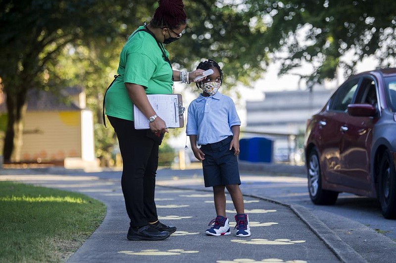 Kimberly Lewis, an instructional assistant at Martin Luther King, Jr. Magnet Elementary School, checks a Pre-K student's temperature as they leave their parent's car on the first day of class on Monday, Aug. 24, 2020.