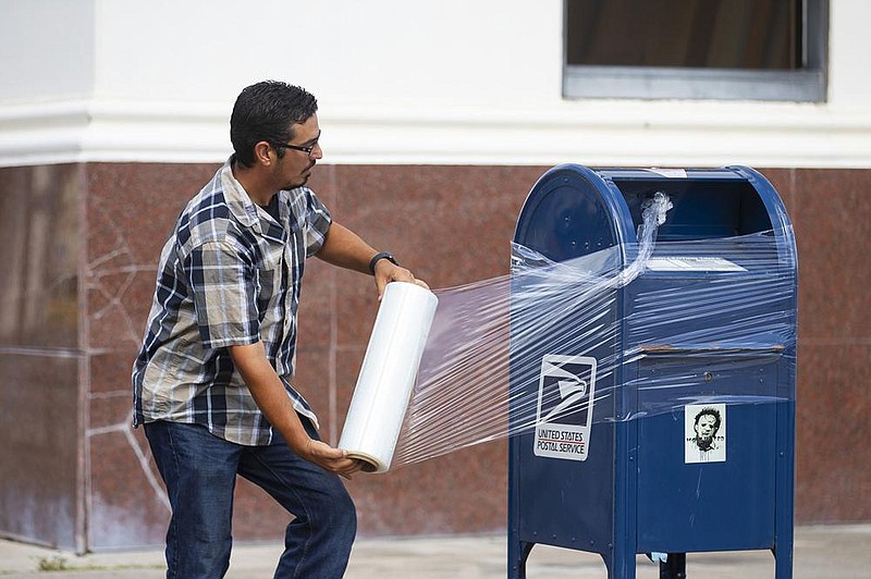 A U.S. Postal Service employee covers a mailbox with plastic wrap Tuesday in Galveston, Texas, to prepare for Hurricane Laura. More photos at arkansasonline.com/826laura/. (AP/Houston Chronicle/Mark Mulligan) 