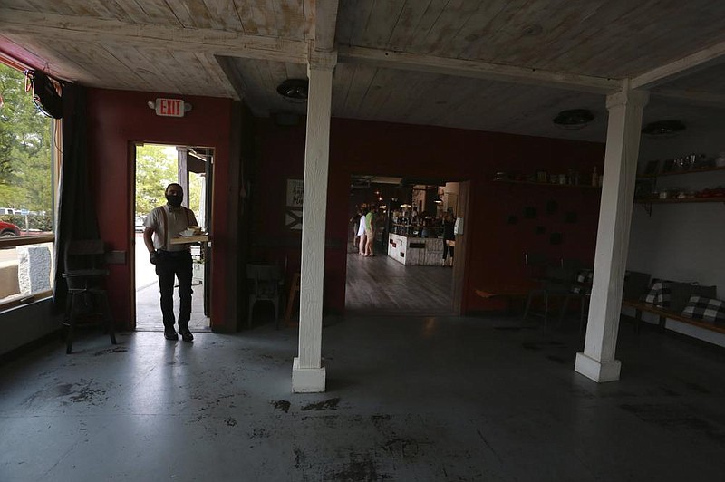A waiter carries dishes from a dining area to the kitchen Monday at the Clafoutis restaurant in Santa Fe, N.M., where tables and chairs were cleared out and a tent was rented to offer dining after indoor seating was banned because of covid-19.
(AP/Cedar Attanasio)
