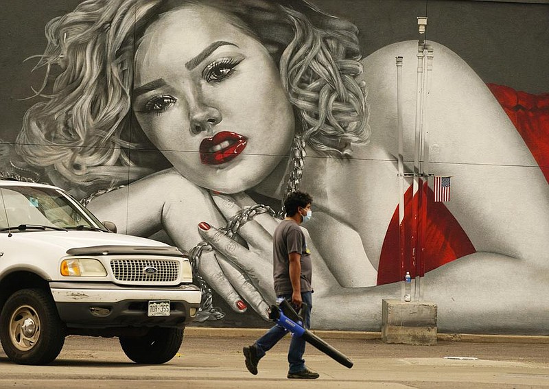 A maintenance worker uses a leaf blower to clean a gas station parking lot Saturday in Denver near a mural on the side of a jewelry store. (AP/David Zalubowski) 