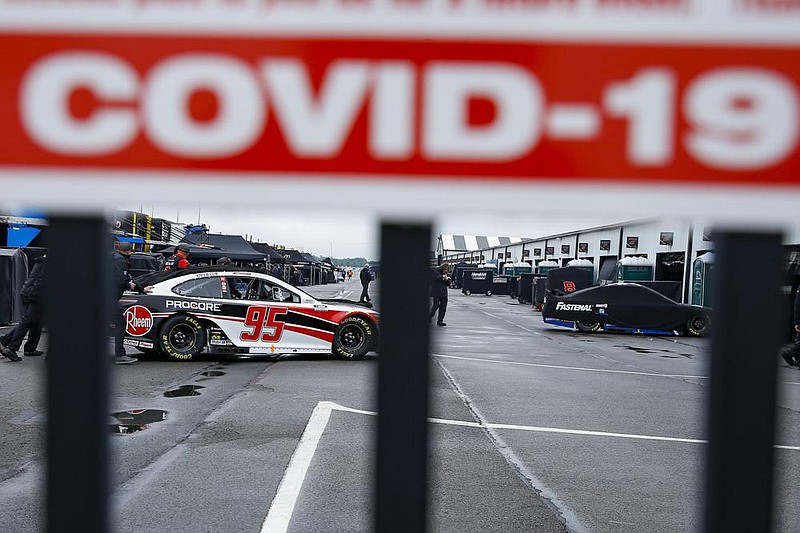 Crew members are visible under a covid-19 alert sign as they push the car of Christopher Bell through the garage area before a scheduled NASCAR Cup Series race in June at Pocono Raceway in Long Pond, Pa. NASCAR will not grant covid-19 relief during the playoffs, which means a positive coronavirus test will end a driver’s championship bid.
(AP/Matt Slocum)