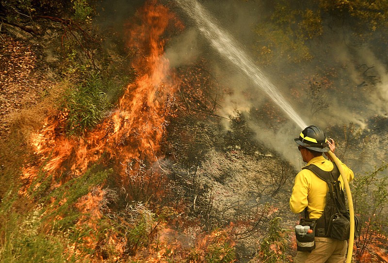 A firefighter puts out a hot spot along Highway 38 northwest of Forrest Falls, Calif., as the El Dorado Fire continued to burn Thursday afternoon, Sept. 10, 2020.