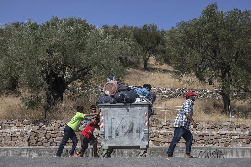 Migrants use a trash bin Friday to move their belongings from the burned Moria refugee camp to a new army-built facility at Lesbos, Greece.
(AP/Petros Giannakouris)