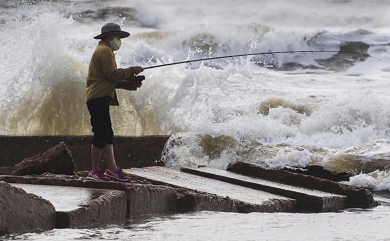 Waves crash as Houston resident Tinh Pham fishes from the rocks at Diamond Beach on the west end of the Galveston Seawall in Galveston, Texas on Saturday, Sept. 19, 2020. Tropical Storm Beta continues to move through the Gulf of Mexico and is expected to bring tidal surge and heavy rain to the area. (Stuart Villanueva/The Galveston County Daily News via AP)