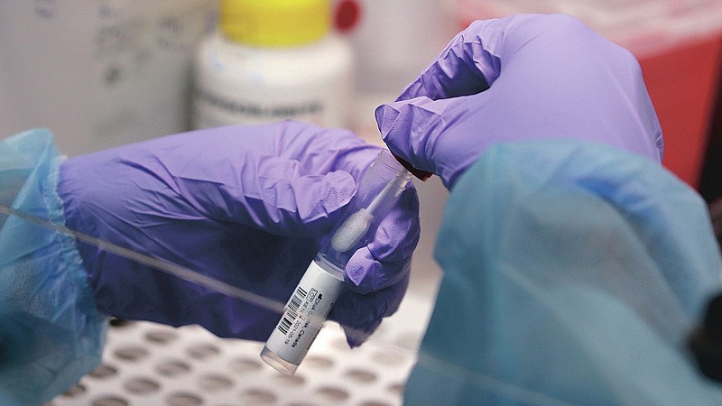 FILE - In this Thursday, July 23, 2020 file photo, a biomedical engineering graduate student handles a swab and specimen vial in a new covid-19 on-campus testing lab in Boston.