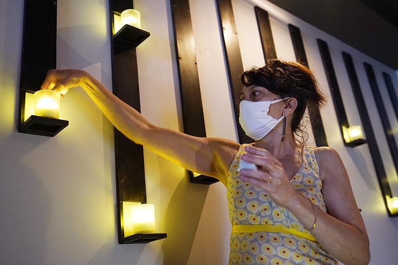 Mama Fox owner Samantha DiStefano installs electric tea lights in preparation for indoor dining at her bar and restaurant, Tuesday, Sept. 29, 2020, in the Bedford-Stuyvesant neighborhood of Brooklyn, in New York. Some lights were dead because they haven't been used in six months when Mama Fox closed during the viral pandemic. New York restaurants may reopen for indoor dining on Wednesday, but with capacity restricted to 25%. "It's baby steps. The 25% gives you the opportunity to dip your toe in," DiStefano said. (AP Photo/Kathy Willens)

